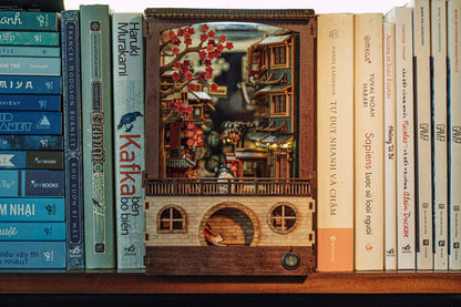 JiuFen Old Street book nook DIY kit assembled on a bookshelf with surrounding books, showcasing a miniature Taiwanese town scenery.